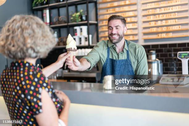 friendly worker at the ice cream parlor handing an ice cream to senior woman smiling - ice cream parlour stock pictures, royalty-free photos & images