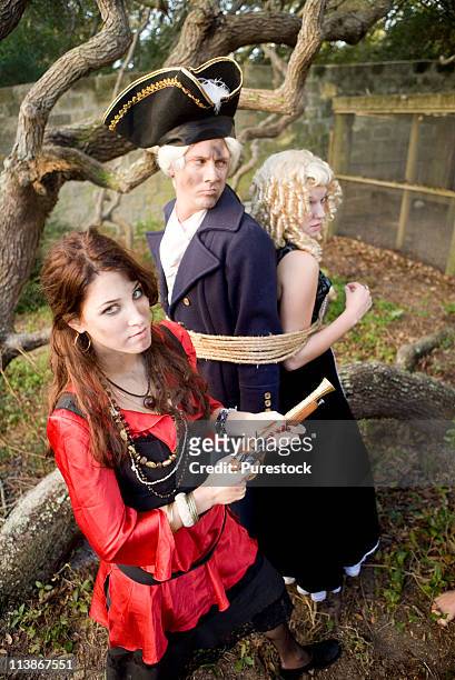portrait of a woman pirate armed with a pistol holding a navy officer and princess captive - princess pirates stock pictures, royalty-free photos & images