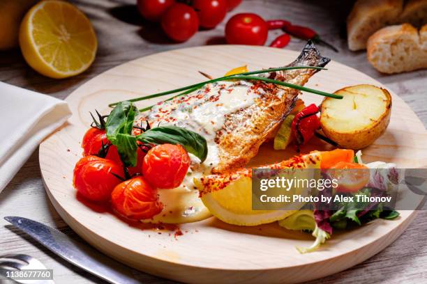 sea bass prepared with potato grilled vegetables served on wooden board close up image - mediterran menü stock-fotos und bilder