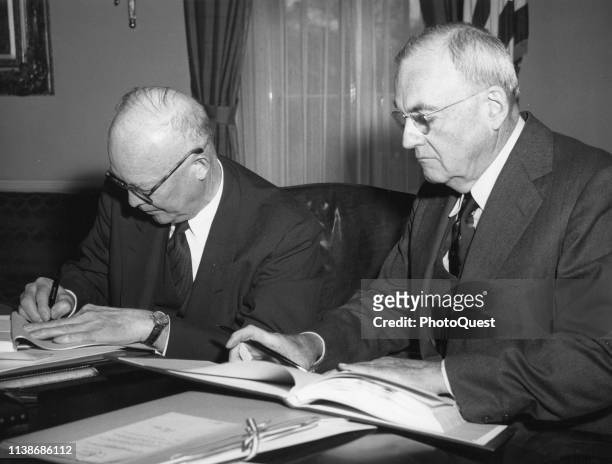 In the White House, American politician US President Dwight D Eisenhower signs the Paris Agreements as US Secretary of State John Foster Dulles waits...