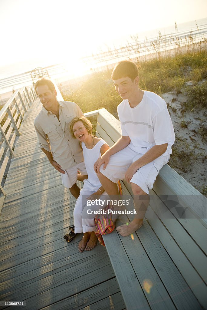 Family sitting on wooden pier at beach at sunrise