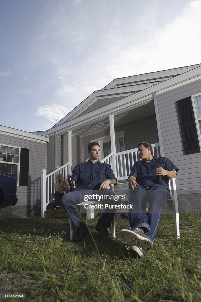 Men sitting and holding drink bottles in front yard of trailer home