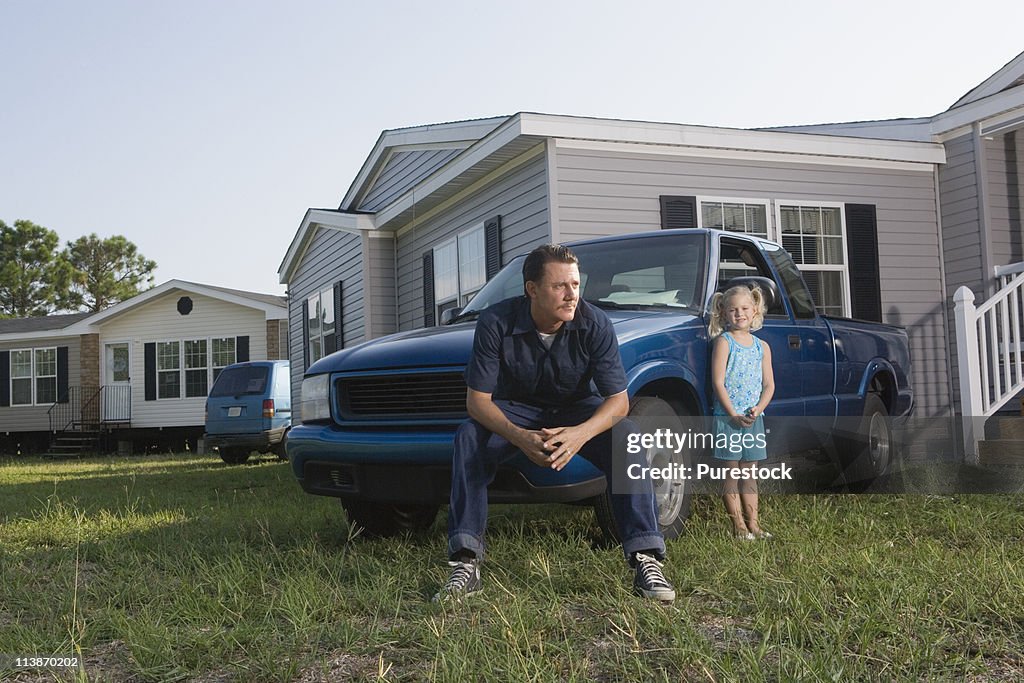 Man sitting on old truck in front of trailer home with daughter