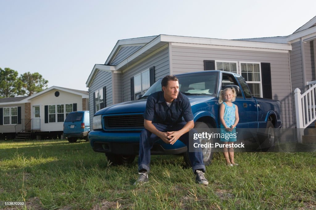 Man sitting on old truck in front of trailer home with daughter