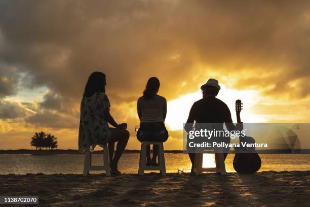 kleine groep vrienden drinken whisky bij de zee bij zonsopgang. - fabolous musician stockfoto's en -beelden