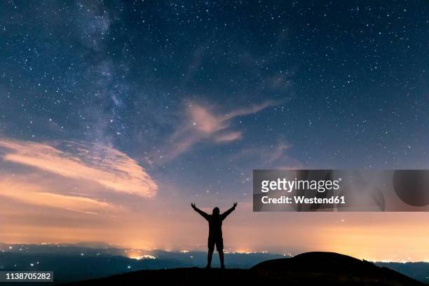 italy, monte nerone, silhouette of a man looking at night sky with stars and milky way - arms raised to sky stock pictures, royalty-free photos & images