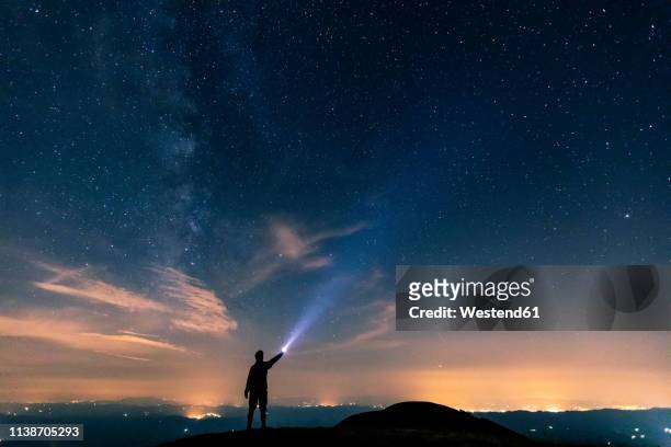 italy, monte nerone, silhouette of a man with torch under night sky with stars and milky way - obiettivo foto e immagini stock