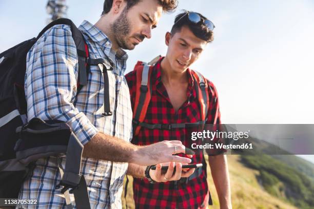 italy, monte nerone, two men hiking and looking at smartphone in mountains - two young men stock pictures, royalty-free photos & images
