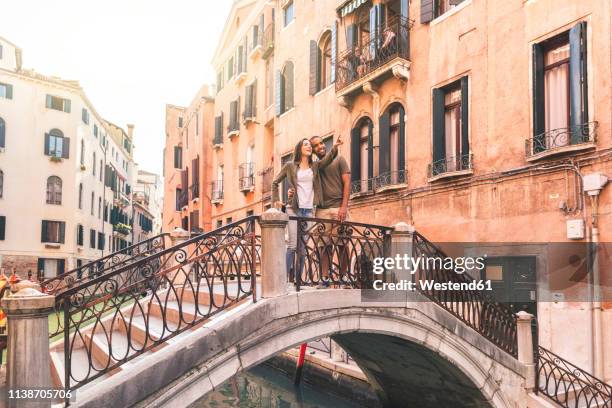 italy, venice, young couple standing on a small bridge exploring the city - venice couple stockfoto's en -beelden