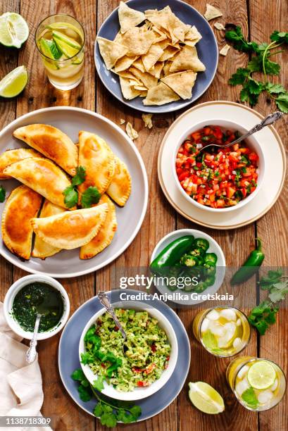 traditional mexican food - meat empanadas with cilantro chimichurri sauce,  guacamole, salsa, tortilla chips and mojito - latin american culture stock pictures, royalty-free photos & images