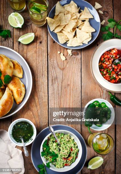 traditional mexican food - meat empanadas with cilantro chimichurri sauce,  guacamole, salsa, tortilla chips and mojito - mexican food on table stock pictures, royalty-free photos & images
