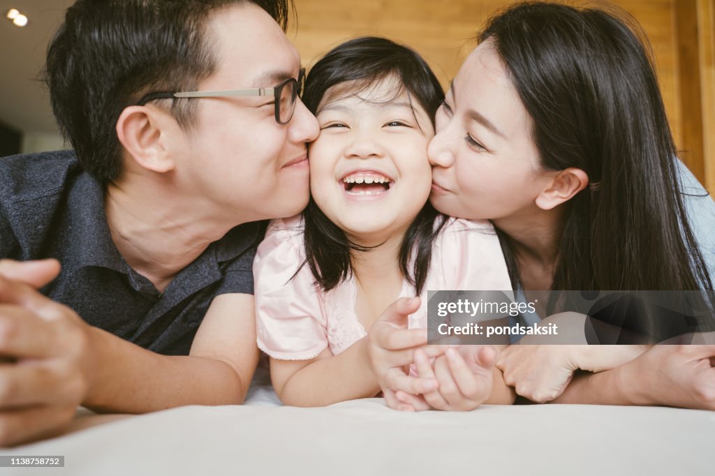 Padres asiáticos besando a su hijita en ambas mejillas. Retrato familiar.