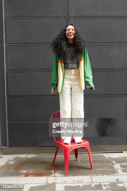 happy woman standing on red chair - bright colour chair stock pictures, royalty-free photos & images