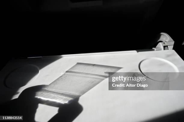 shadow of hand holding a transparent glass in an airplanes seat table. - in tischhöhe stock-fotos und bilder