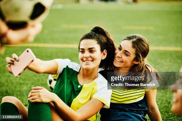 Female soccer players taking selfie with smart phone while sitting on field after match