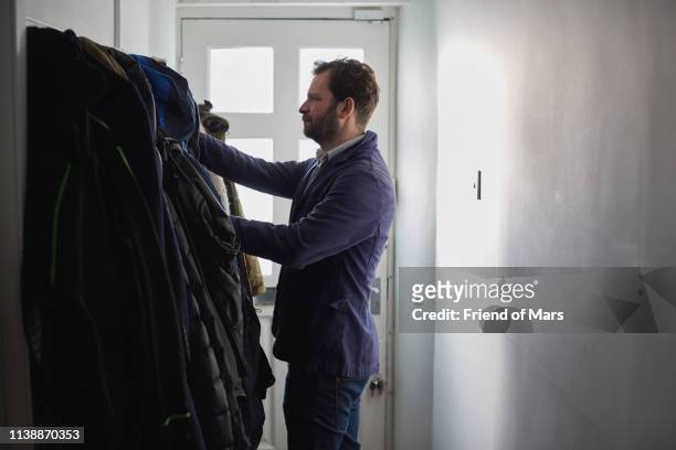man picks a coat and scarf getting ready to leave home. - coat rack stock pictures, royalty-free photos & images