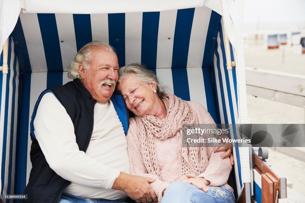 Portrait of a senior couple sitting at the beach in a hooded beach chair embracing