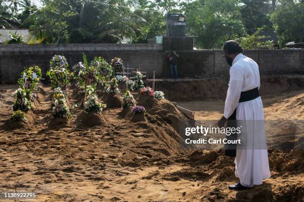 Priest pauses next to graves after a mass funeral near St Sebastian's's Church on April 23, 2019 in Negombo, Sri Lanka. At least 321 people were...