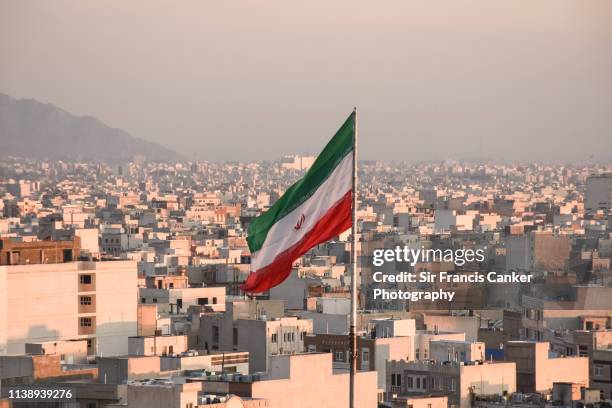 iranian flag waving with city skyline on background in tehran, iran - revolutionary war flag stock-fotos und bilder