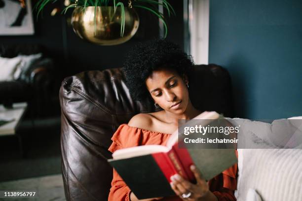 portrait of a young woman relaxing and reading in her downtown los angeles apartment - black book stock pictures, royalty-free photos & images