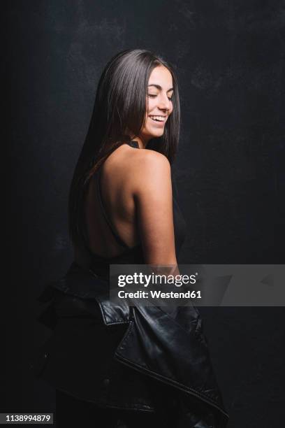 portrait of smiling young woman in evening wear and black leather jacket in front of black background - off the shoulder coat stock pictures, royalty-free photos & images