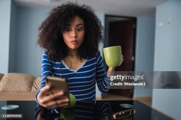 portrait of young woman with mug starring at cell phone - sorpresa fotografías e imágenes de stock