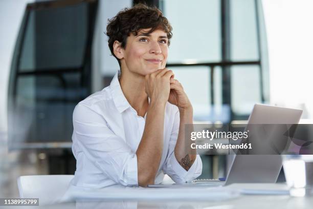 smiling businesswoman sitting at desk in office with laptop - woman business desk front laptop office bildbanksfoton och bilder