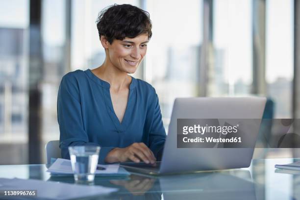 businesswoman sitting at desk in office using laptop - women's short programme stock-fotos und bilder