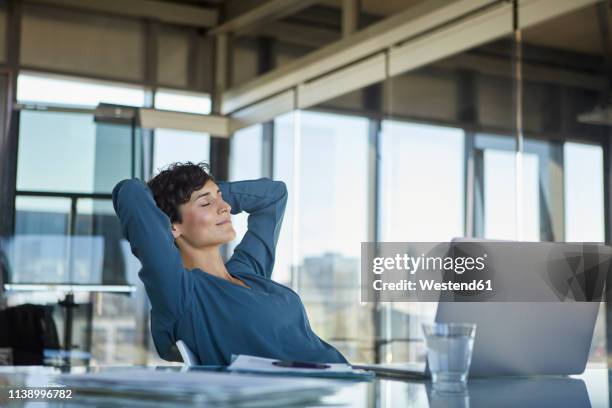 businesswoman sitting at desk in office with closed eyes - hands behind head stock pictures, royalty-free photos & images