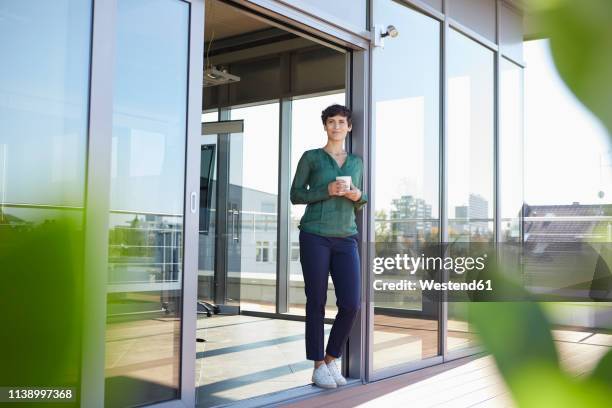 smiling woman standing at the window having a coffee break - city office photos et images de collection