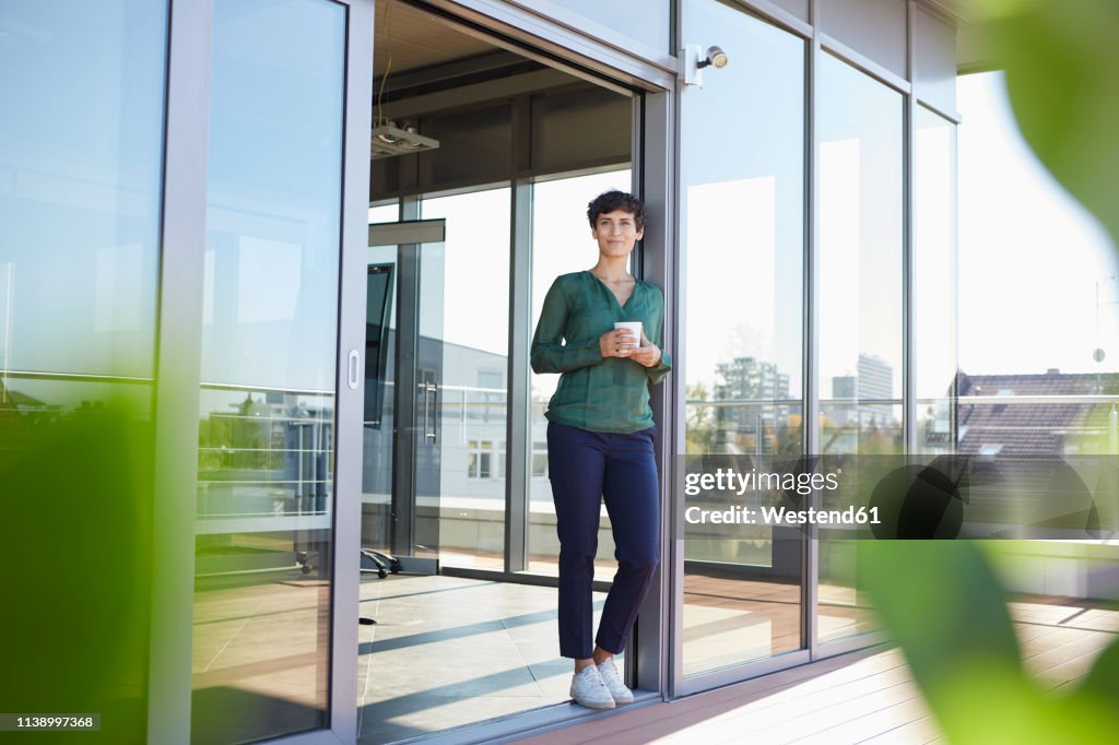 Smiling woman standing at the window having a coffee break