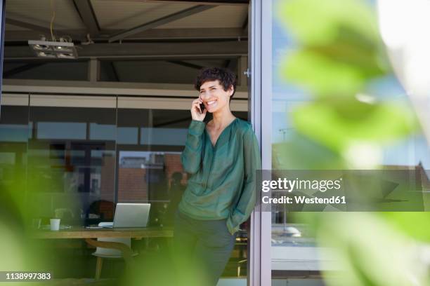 smiling woman standing at the window talking on cell phone - red blouse fotografías e imágenes de stock
