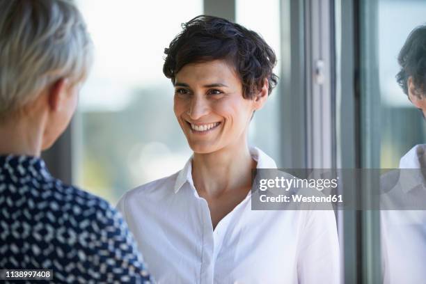 portrait of smiling smiling businesswoman looking at colleague at the window in office - white blouse stock-fotos und bilder