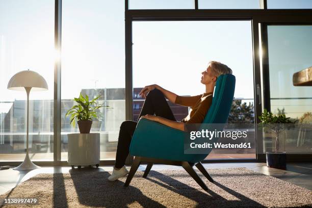 woman sitting in armchair in sunlight with closed eyes - shadow people fitness stockfoto's en -beelden