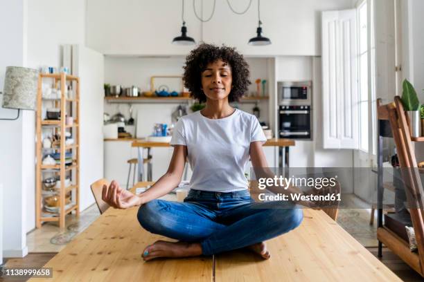 smiling woman with closed eyes in yoga pose on table at home - schneidersitz stock-fotos und bilder