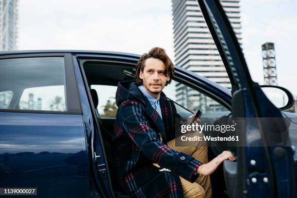 spain, barcelona, man getting out of the car with cell phone in his hand - business man car stock-fotos und bilder