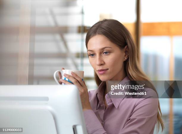 businesswoman in office holding cup looking at pc - purple shirt fotografías e imágenes de stock