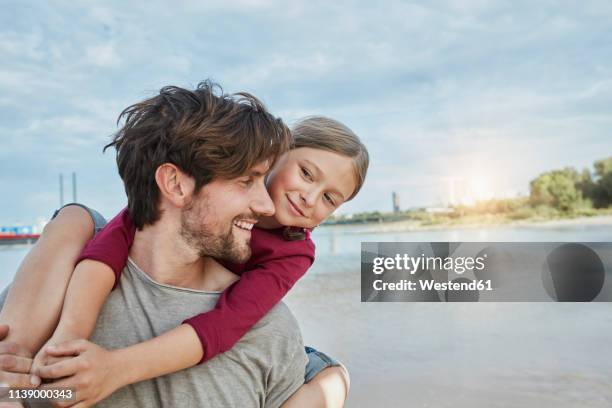 germany, duesseldorf, happy father carrying daughter piggyback at rhine riverbank - düsseldorf stock-fotos und bilder