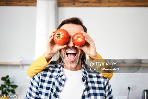 couple having fun in the kitchen, playing with tomatoes - mischief woman stock pictures, royalty-free photos & images