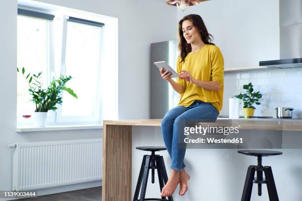 woman sitting on kitchen counter at home, using digital tablet - smart windows photos et images de collection