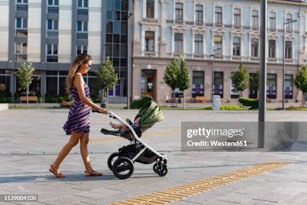 mother pushing baby in a stroller in the city - stroller stock pictures, royalty-free photos & images