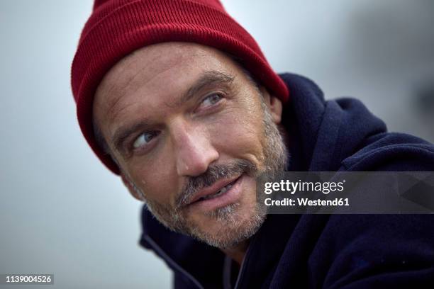 portrait of bearded mature man wearing red cap outdoors - winter hat stock pictures, royalty-free photos & images