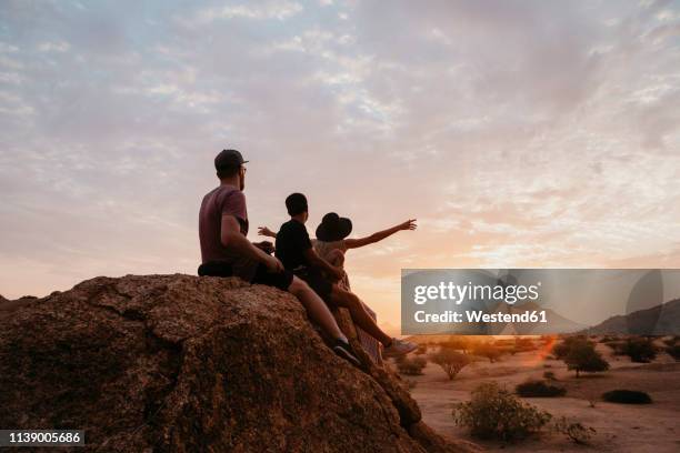 namibia, spitzkoppe, friends sitting on a rock watching the sunset - outdoor guy sitting on a rock stockfoto's en -beelden