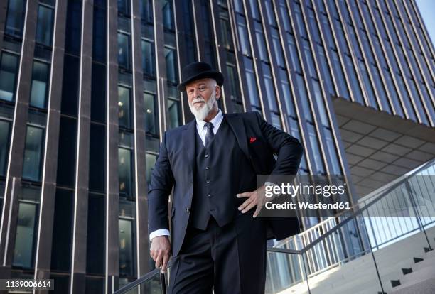 elegant businessman with bowler hat and walking cane, standing on stairs in the city - bowler hat stock pictures, royalty-free photos & images