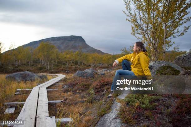 finland, lappland, kilpisjaervi, woman sitting at wooden boardwalk - moore stock-fotos und bilder