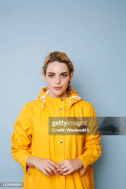 portrait of young woman wearing yellow rain coat in front of blue background - レインコート ストックフォトと画像