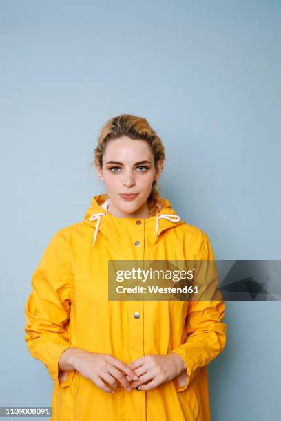 portrait of young woman wearing yellow rain coat in front of blue background - oil skin stock pictures, royalty-free photos & images