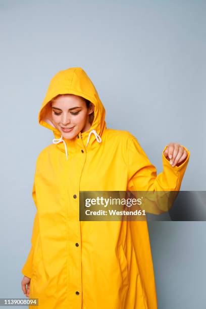 smiling young woman wearing yellow rain coat in front of blue background dancing - raincoat stock-fotos und bilder