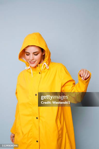 smiling young woman wearing yellow rain coat in front of blue background dancing - regnkläder bildbanksfoton och bilder