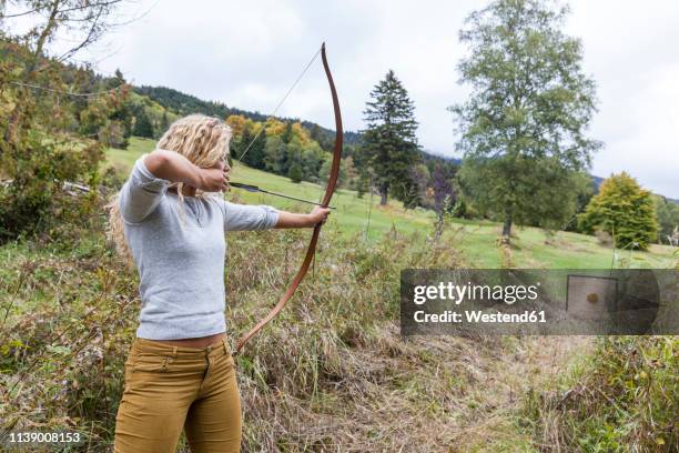 archeress aiming with her bow on target - pfeil und bogen stock-fotos und bilder